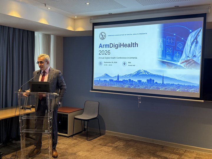 Prof. Georgi Chaltikyan speaking beside the ArmDigiHealth-2026 conference banner